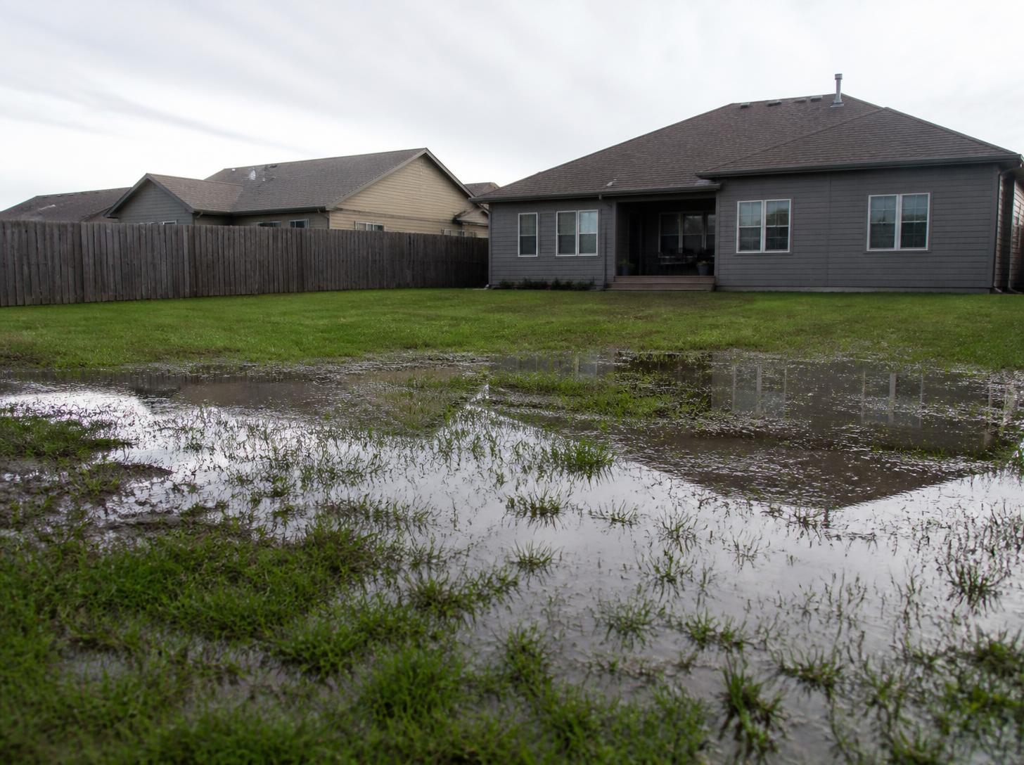 Water pooling on clay soil that won't drain in a Kansas backyard
